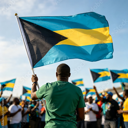Back view of a man holding and waving the Bahamas flag high during a public holiday celebration or rally.