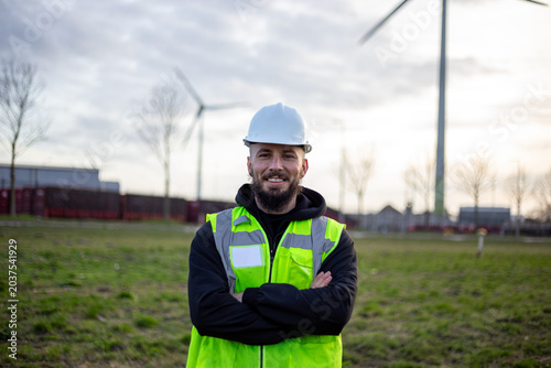Photography Electrical technician standing confidently at clean energy site with wind turbin