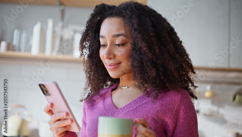Portrait woman browsing smartphone message holding morning coffee at kitchen.
