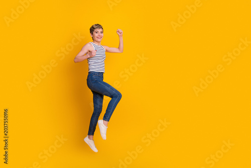 Foto Happy young woman jumping in casual jeans and striped top against a bright yello