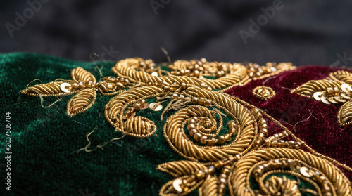 Luxurious embroidered fabric featuring intricate gold designs on rich green and burgundy velvet