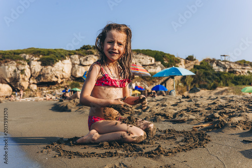 Konstfotografi Little girl playing with wet sand on beach during summer family vacation by the