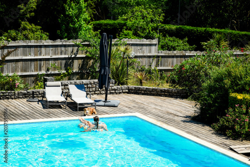 Beautiful young girl enjoying relaxing in the pool during a heatwave with her dog