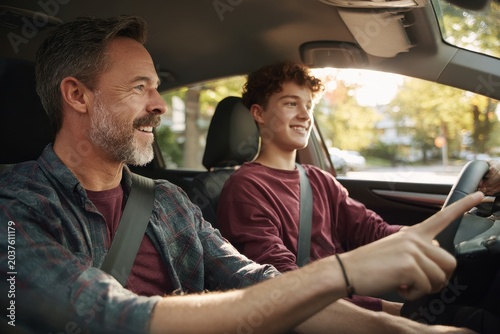 Patient instruction: father coaching his teenage son to drive with a smile