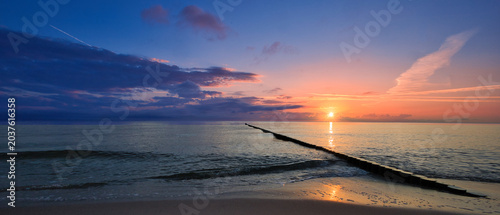Quadro su tela Panoramic sunrise over the Baltic Sea beach with wooden groynes and golden refle