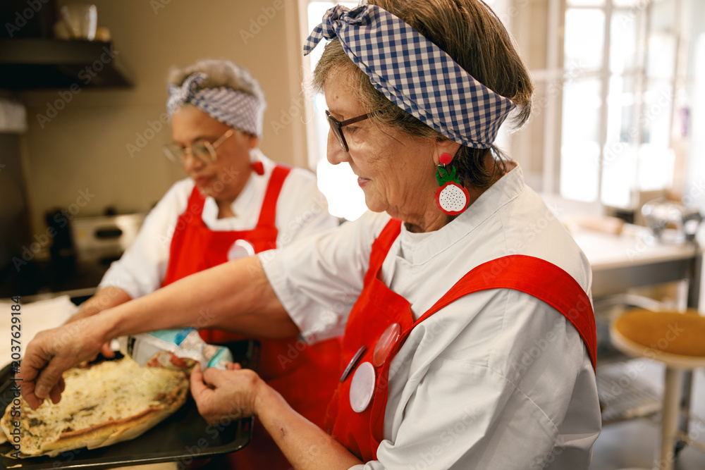Obraz premium Two Caucasian elderly women cooking in bright natural lighting with a cheerful wholesome and fun community vibe