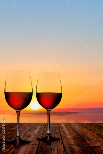 Zwei Rotweingläser auf einer Veranda bei Sonnenunteragn am Meer