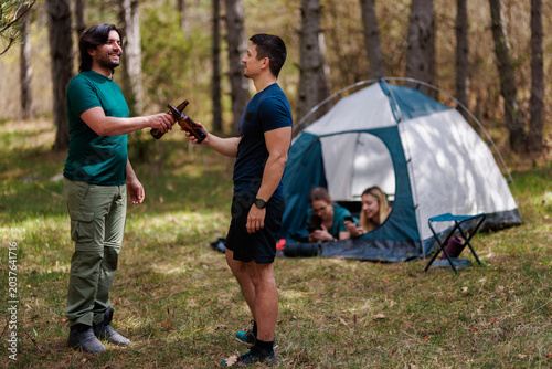 Fotografía Friends enjoying a camping trip in the forest, sharing drinks and laughter near