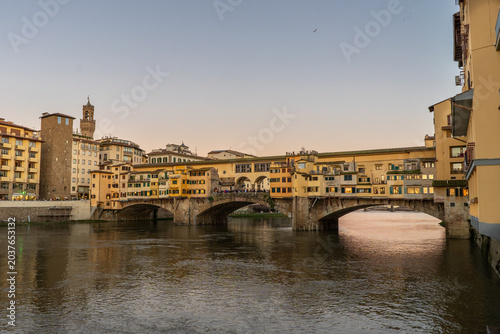 The iconic Ponte Vecchio bridge in Florence, Italy, glows with warm light during a serene sunset over the Arno River