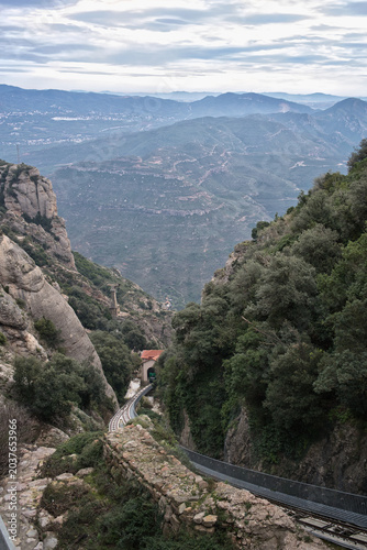 A scenic view of the Montserrat mountain railway winding through lush green slopes and rocky terrain towards a tunnel