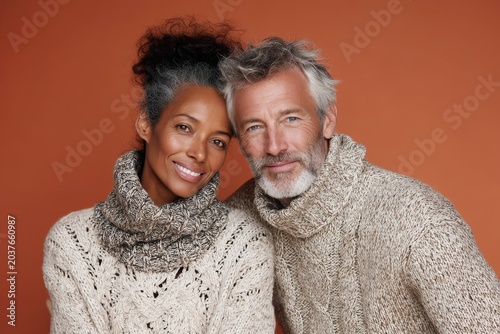 Portrait of a smiling multiethnic couple in their 60s wearing a classic turtleneck sweater in front of soft orange background
