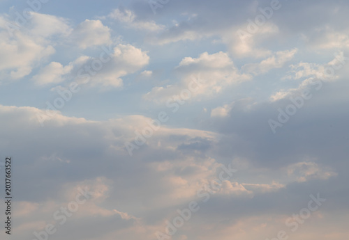 The sky unfolds in a painterly gradient, where fading azure meets a gentle amber horizon. Luminescent clouds, feathered in pearl and peach, drift across this ethereal canvas as deeper shadows of laven
