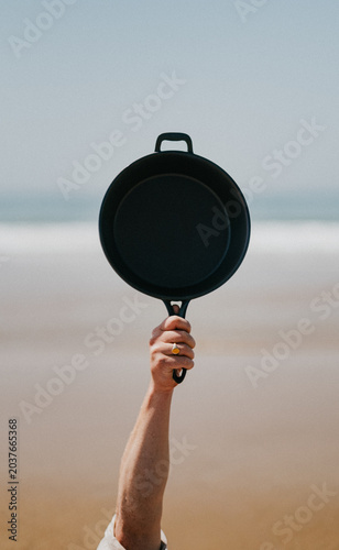 Photos Hand holds frying pan aloft against beach backdrop