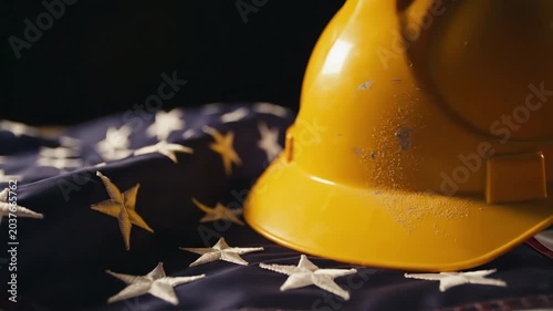 Yellow hard hat resting on a folded American flag, representating Labor Day of USA