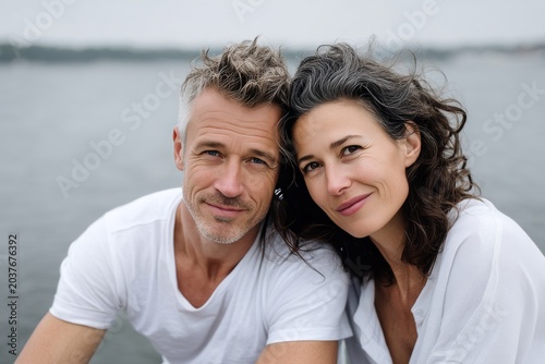 Portrait of a content couple in their 40s wearing a simple cotton shirt over calm bay background