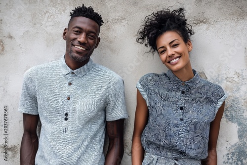 Portrait of a satisfied multicultural couple in their 20s donning a classy polo shirt isolated on bare concrete or plaster wall