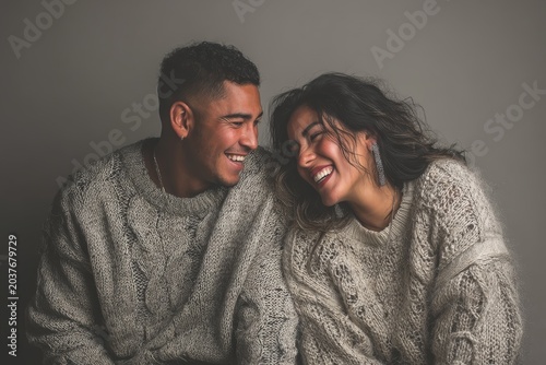 Portrait of a grinning latino couple in their 30s dressed in a warm wool sweater over plain cyclorama studio wall