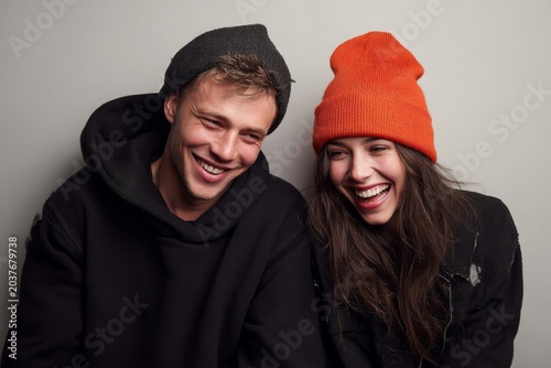 Portrait of a grinning caucasian couple in their 20s sporting a trendy beanie isolated in plain cyclorama studio wall