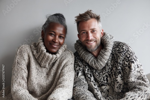 Portrait of a smiling multicultural couple in their 40s dressed in a warm wool sweater isolated in crisp minimalistic living room