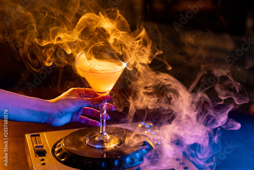 Canvastavla Hand holding smoky orange cocktail on DJ deck in dramatic neon bar atmosphere