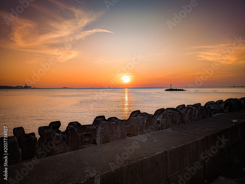 Foto Serene coastal landscape at dawn with a calm, mirror-like ocean reflecting the soft glow of the sunrise sky