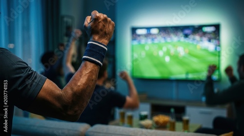 A group of friends excitedly watch a soccer match on television together at home