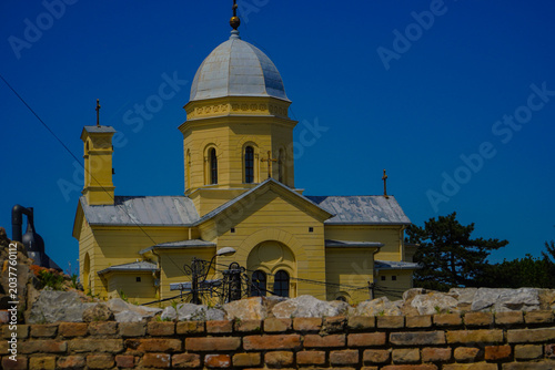 photo of a beautiful church with a yellow facade above which is a blue sky