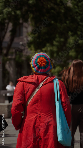 lady in a red coat and colorful hat photographed from behind