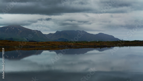 A cloudy, early summer morning at a lake surrounded by the mountains. Reflection of passing clouds on still water; panning time-lapse. Lofoten Islands, Northern Norway.