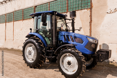 Blue Agricultural Tractor Parked Outdoors Near Industrial Building with Large Rubber Tires