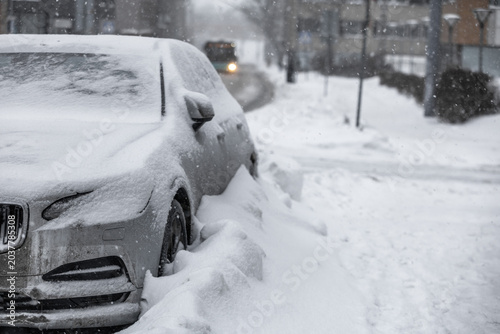 фотографія Snow-covered car parked on Tallinn city street during heavy winter snowfall, thick snowdrifts burying wheels and windshield