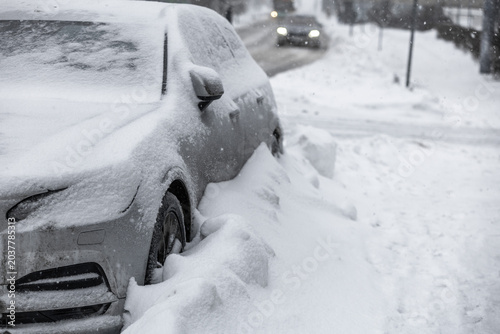 Foto Snow-covered car parked on Tallinn city street during heavy winter snowfall, thick snowdrifts burying wheels and windshield