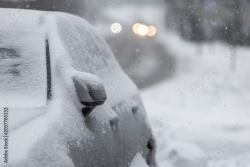 Fotografie Snow-covered car parked on Tallinn city street during heavy winter snowfall, thick snowdrifts burying wheels and windshield