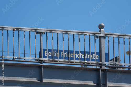 Fotografía A Berlin Friedrichstrasse station sign appears blurred behind a sharp metal railing