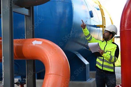 Industrial engineer inspecting large water treatment system equipment at a municipal water plant. Maintenance of pipelines, valves, pumps and storage tanks supporting clean water production and utilit