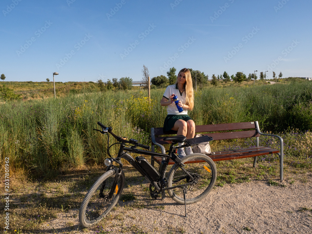 Fototapeta premium Young woman resting on bench after electric bicycle ride