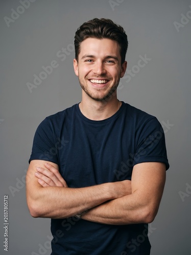 Portrait of confident happy handsome young caucasian man with toothy smile crossing hands in casual blue t-shirt on isolated gray background