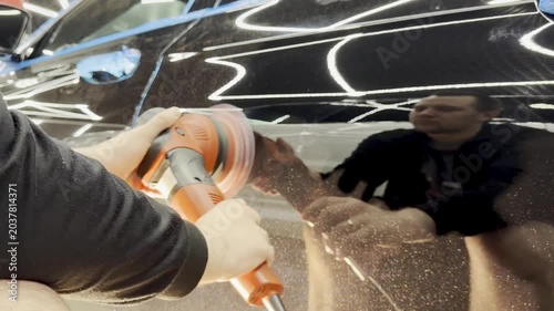 A car service worker polishes the car body with a polishing machine. Detailing and polishing of the car. Car detailing - hands with an orbital polishing machine in an auto repair shop. 