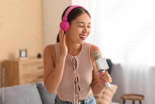 Beautiful young happy Asian woman in headphones with microphone singing while...