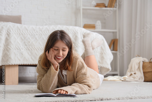 Young woman writing New Year goals on carpet in bedroom