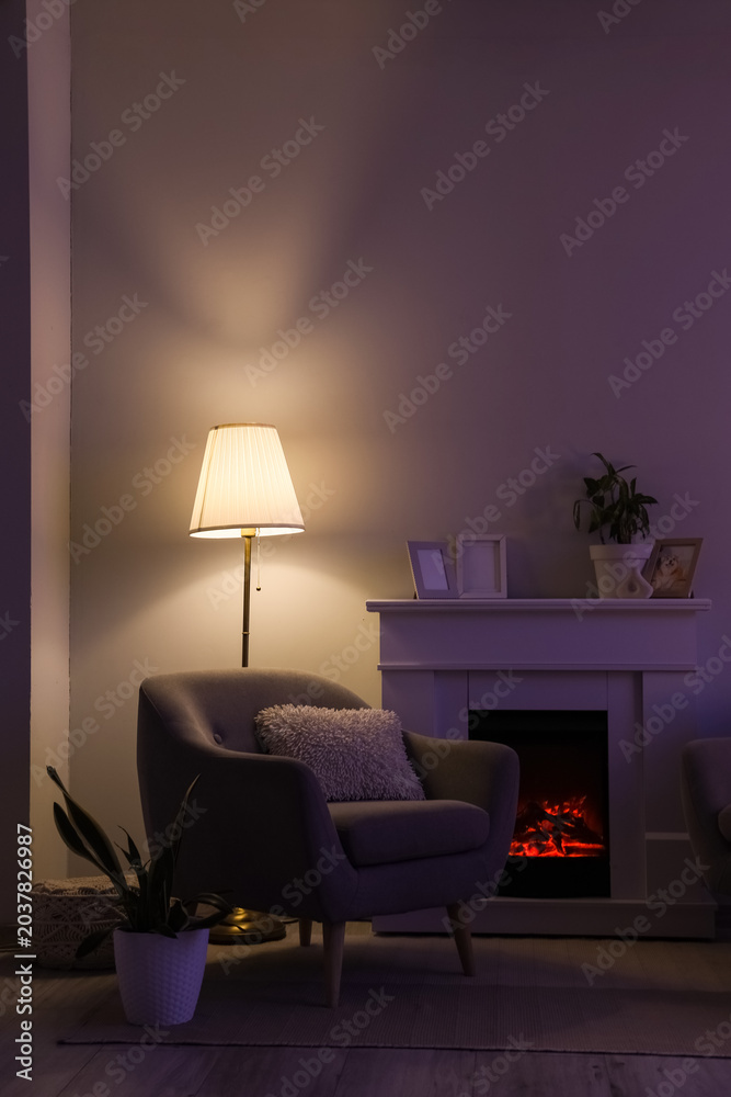 Fototapeta premium Interior of dark living room with glowing lamp, armchair and fireplace at night