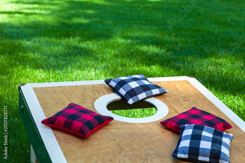 Low angle view of a corn hole board on grass with plaid bean bags on a sunny summer day