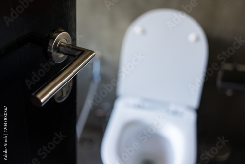 Door with stainless knob door half open in front of interior bathroom clean white toilet with open lid
