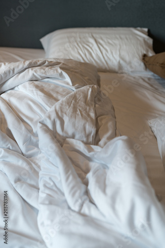 Unmade bed featuring satin sheets and plush pillows with crumpled duvet cover in the morning