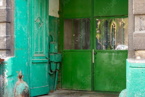 Photos Historic entrance gate and carved wooden doors painted in vibrant green, set in a weathered stone portal of an old tenement house with a vintage electrical box and glass windows