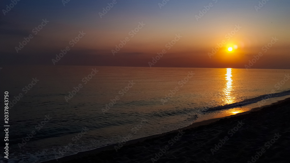 Αυτοκόλλητο Serene sunset over a calm ocean with gentle waves lapping at the sandy shore