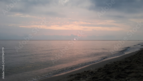 Serene beach sunset with pink and gray hues over calm waters.