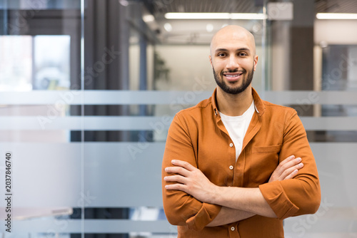 Confident bald man smiling with crossed arms in office