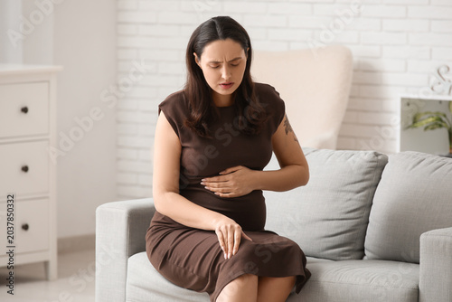 Pregnant young woman suffering from pain in knee on sofa at home