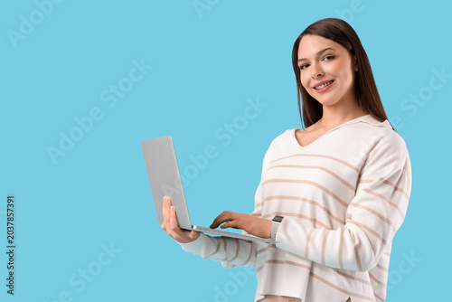 Beautiful young woman with modern laptop on blue background